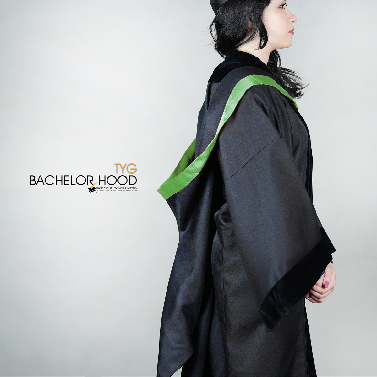 A side view of a graduate in a black graduation gown with a green bachelor hood against a plain background