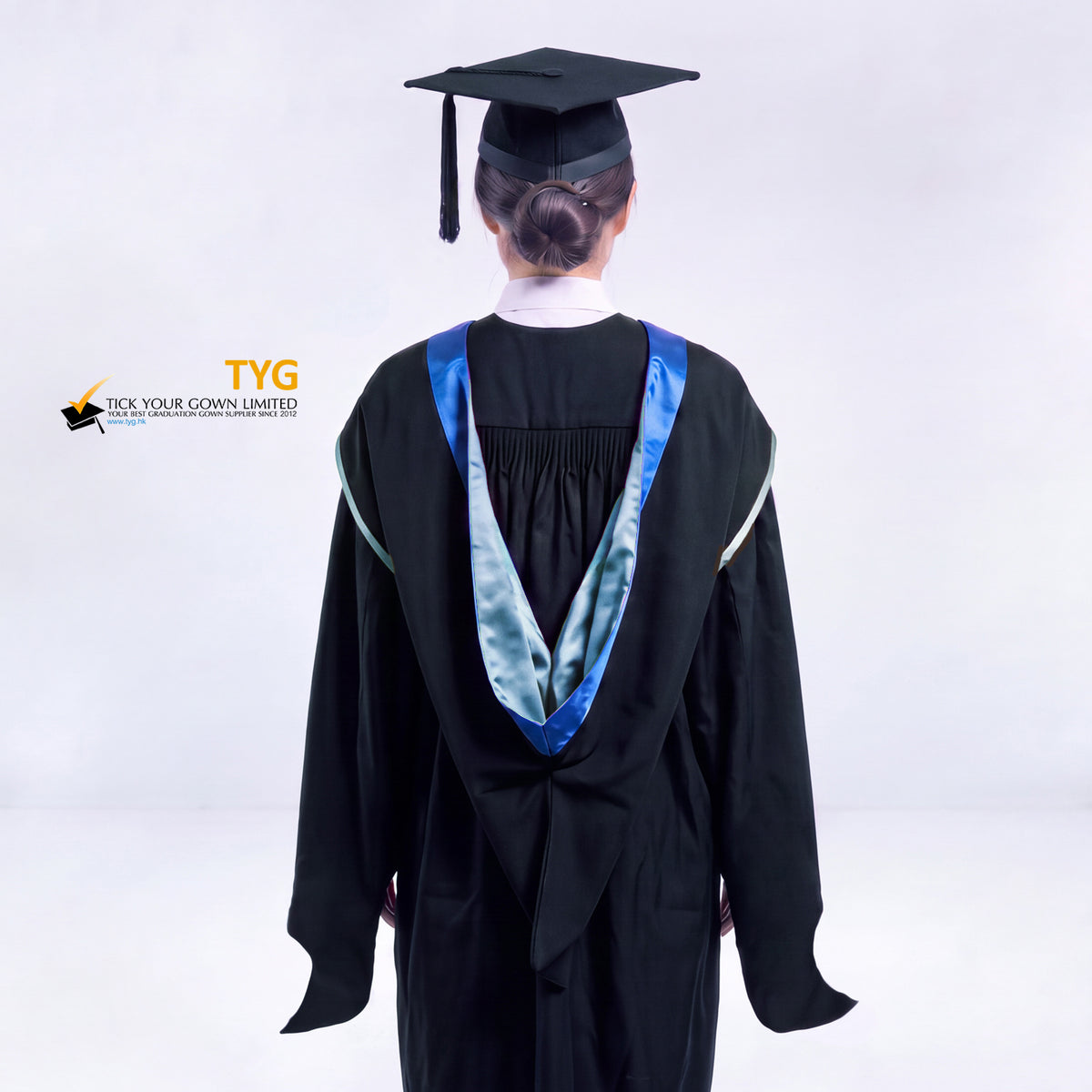A back view of a woman in a black master's graduation gown classic UK with a blue hood with sky blue trim accent and with a black mortarboard cap with a black tassel against a gray background.