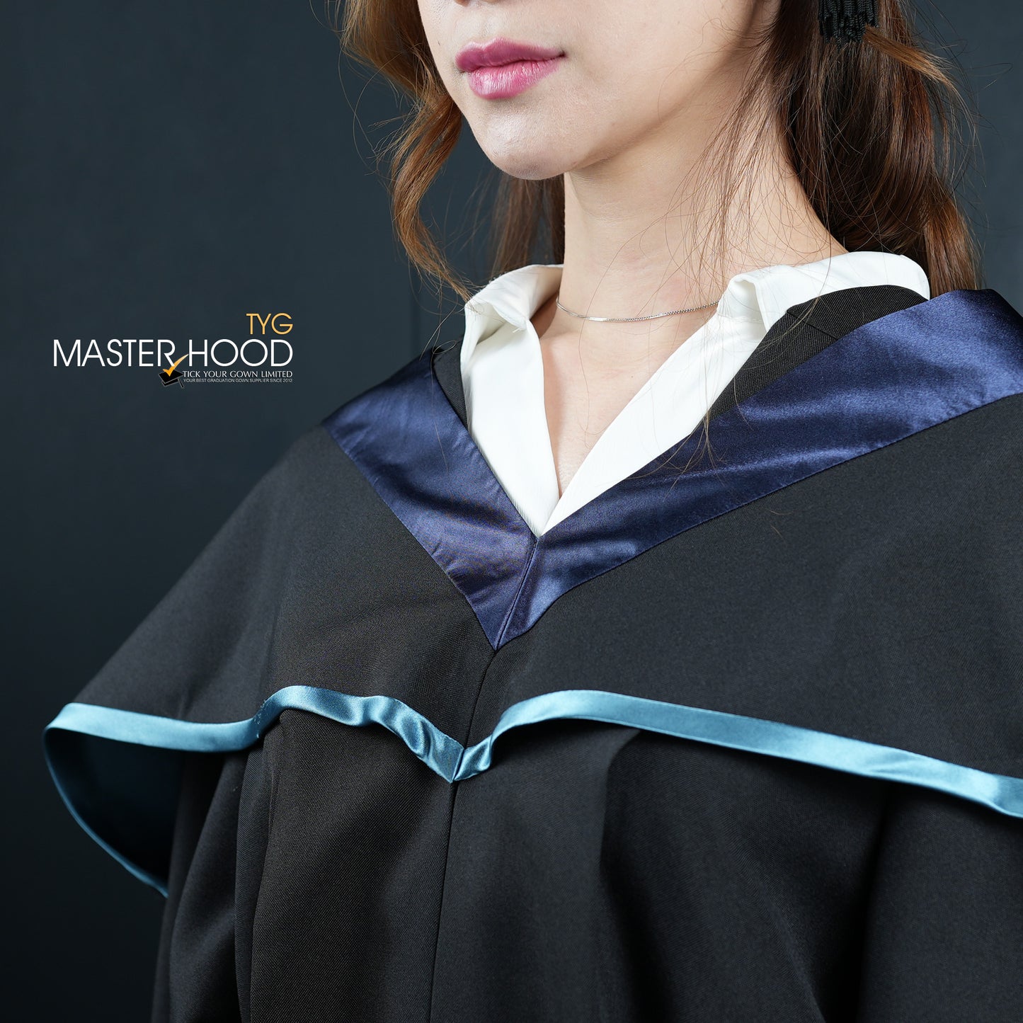 Profile view of a person wearing a black graduation gown and hood with a light blue trim on a dark background
