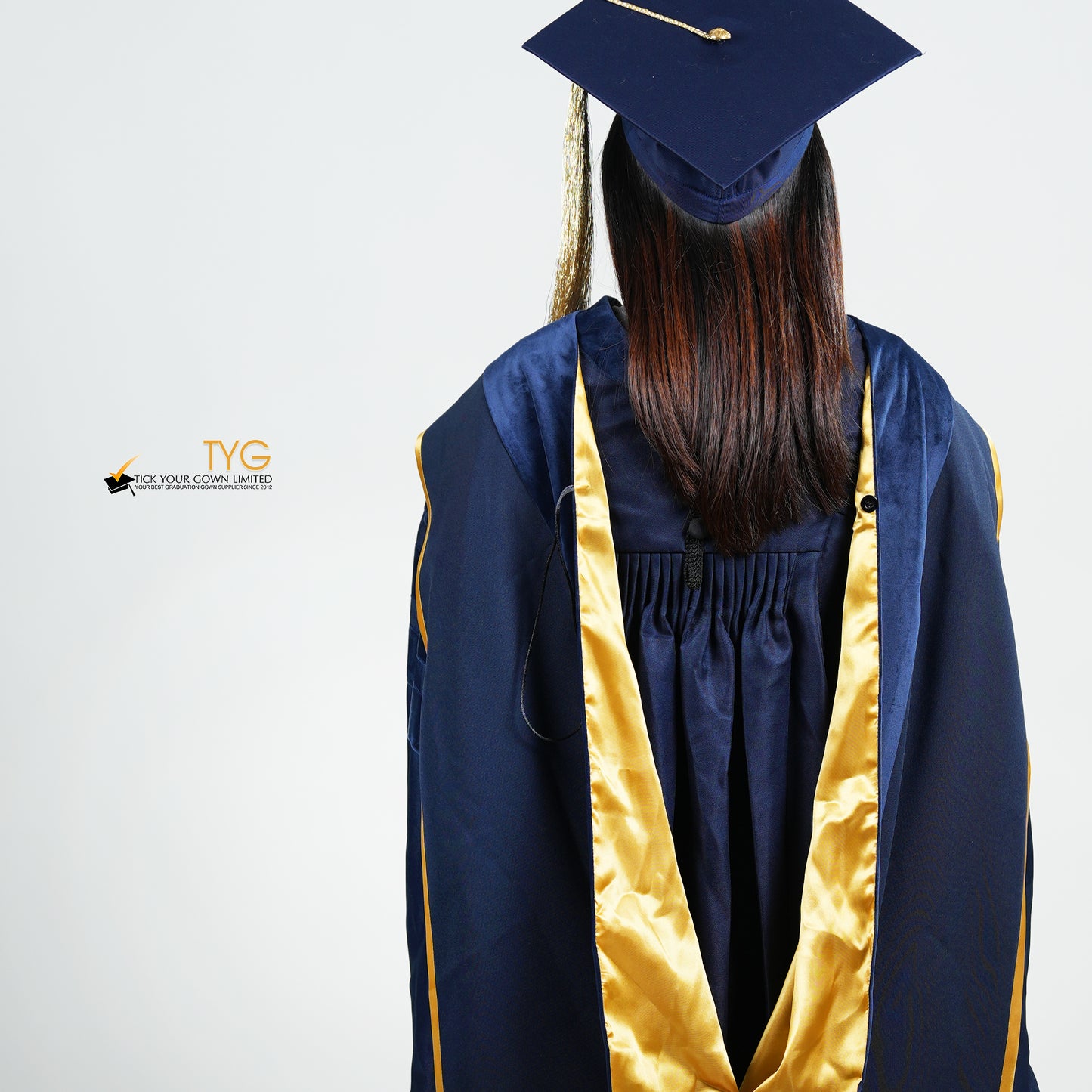 A detailed back view of a person wearing a PhD classic navy blue velvet graduation gown with yellow lining hood, and a navy blue doctoral bonnet with gold tassel.