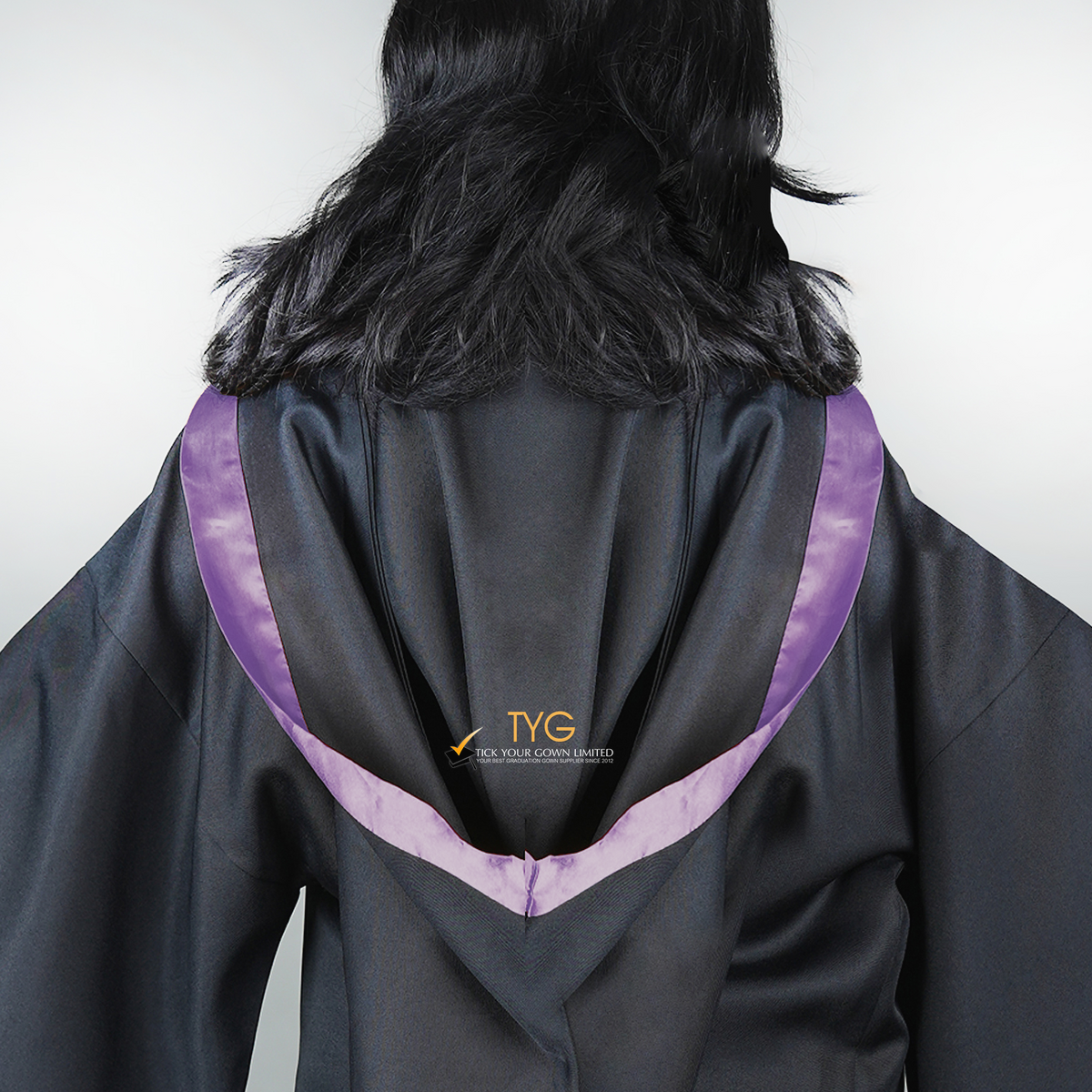 Detailed back view of a graduate in black graduation gown with a light purple bachelor hood against a plain background