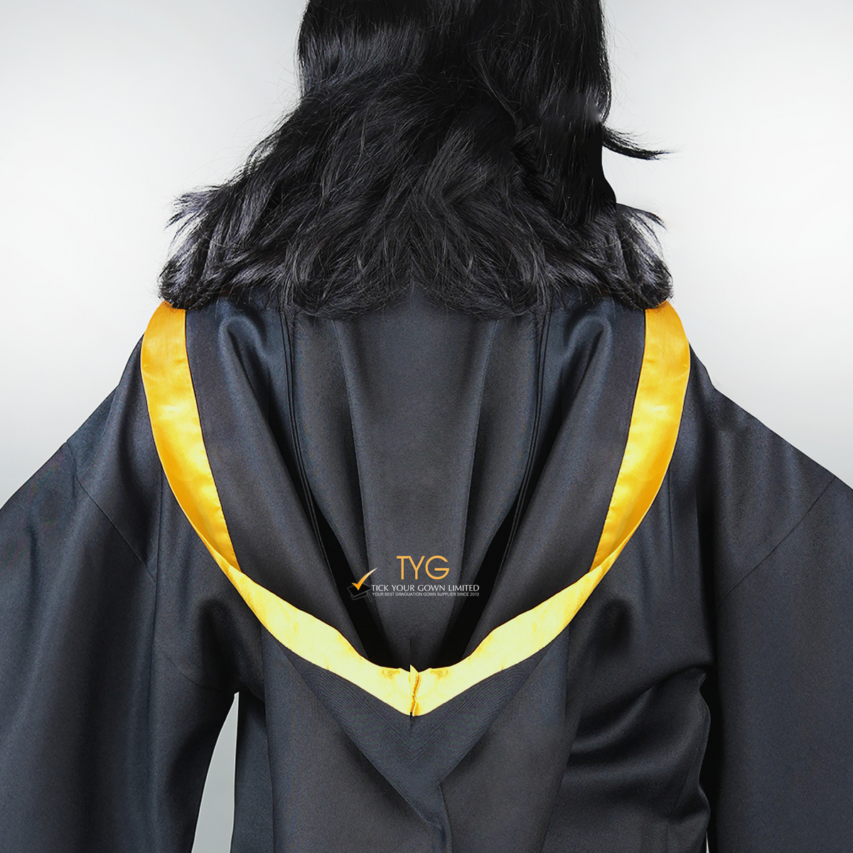 Detailed back view of a graduate in black graduation gown with a yellow bachelor hood against a plain background