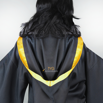 Detailed back view of a graduate in black graduation gown with a yellow bachelor hood against a plain background