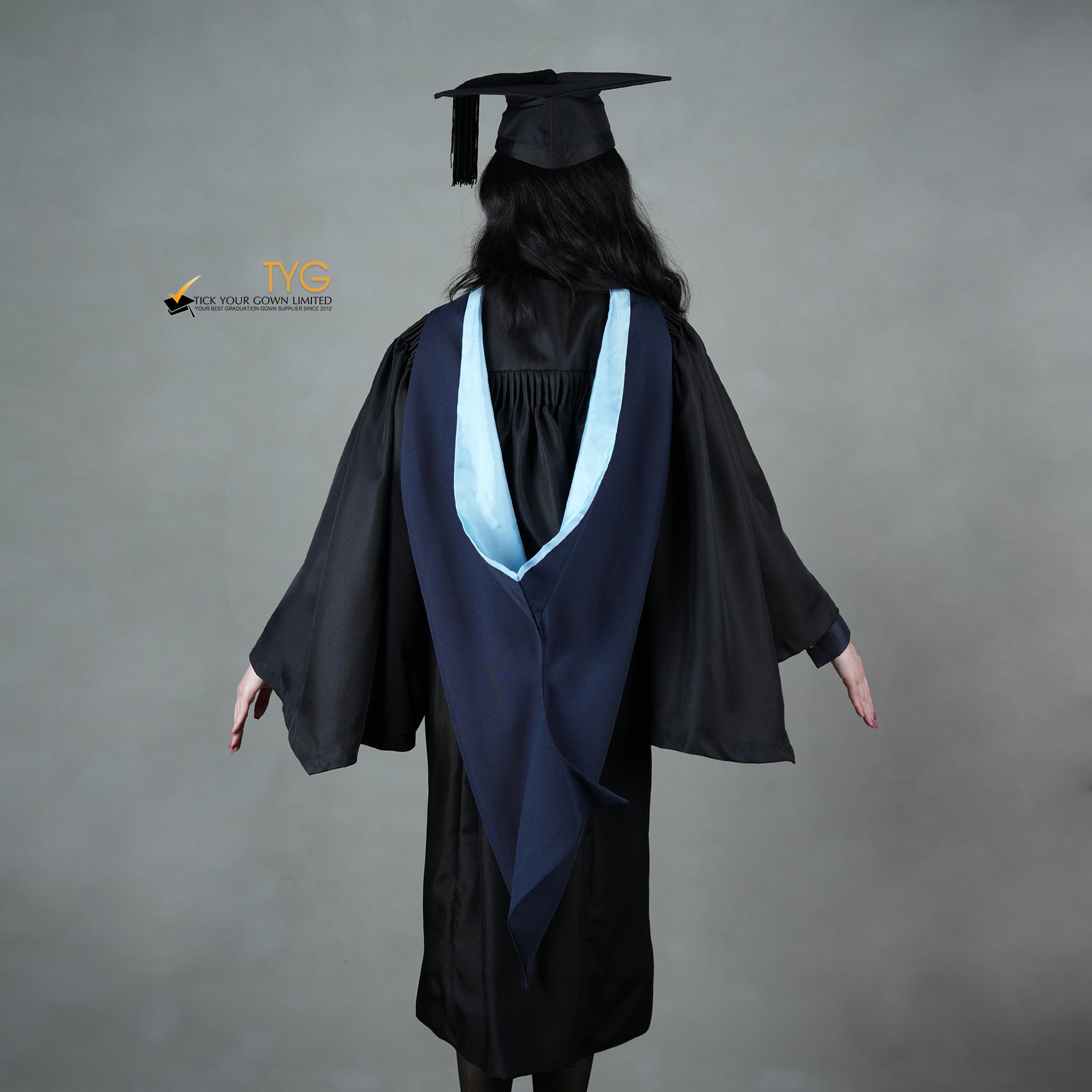 A back view of a graduate in a black cap and gown with a navy blue hood with light blue lining against a gray background