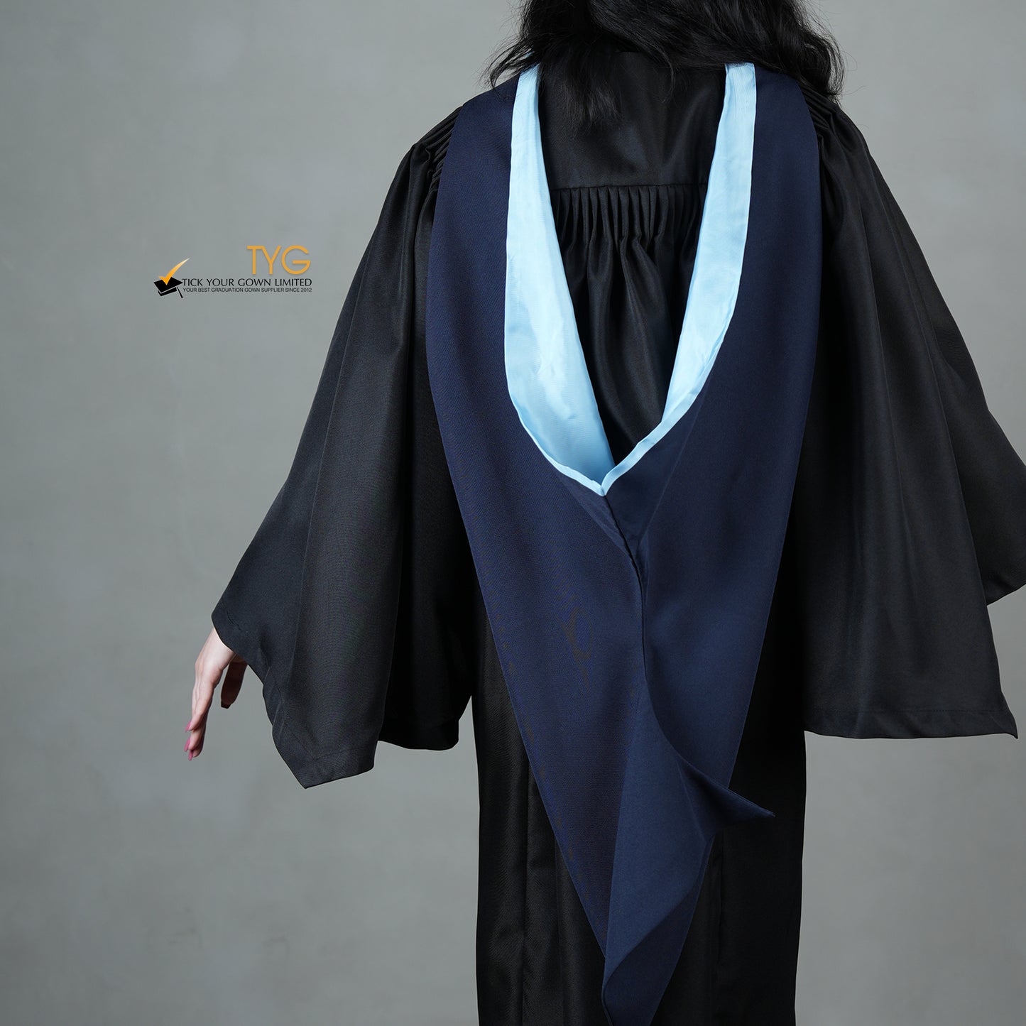 A detailed back view of a graduate in a black gown with a navy blue hood with light blue lining against a gray background