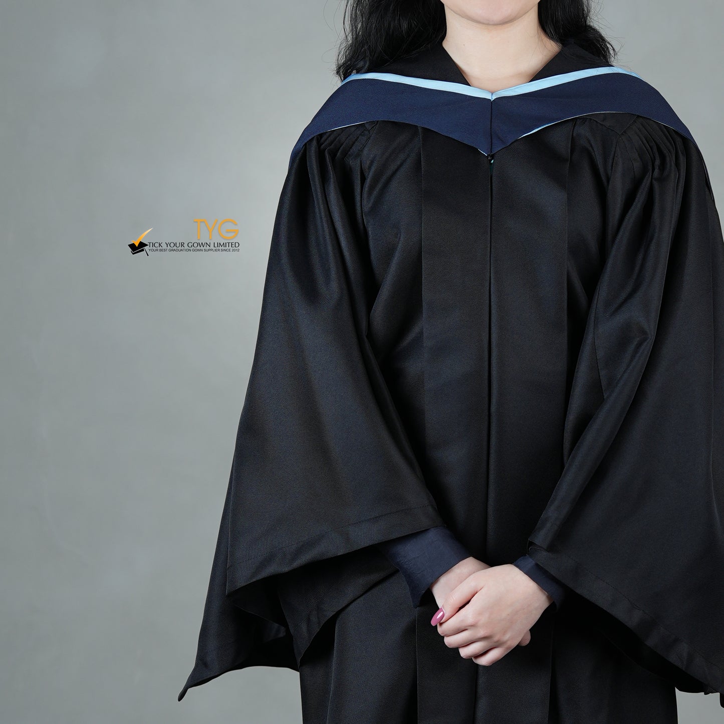 A detailed front view of a graduate in a black gown with a navy blue hood with light blue lining against a gray background