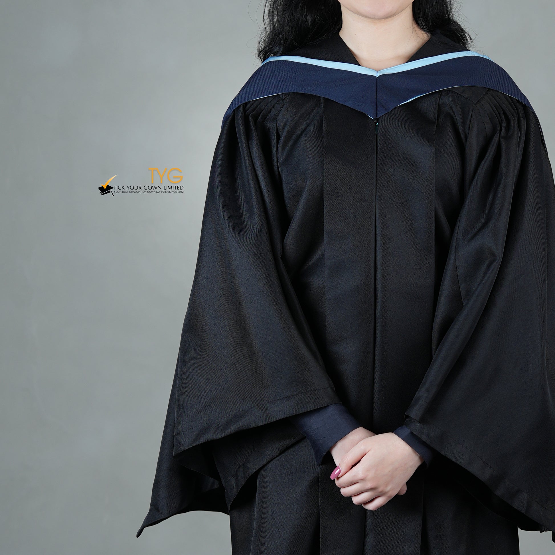 A detailed front view of a graduate in a black gown with a navy blue hood with light blue lining against a gray background