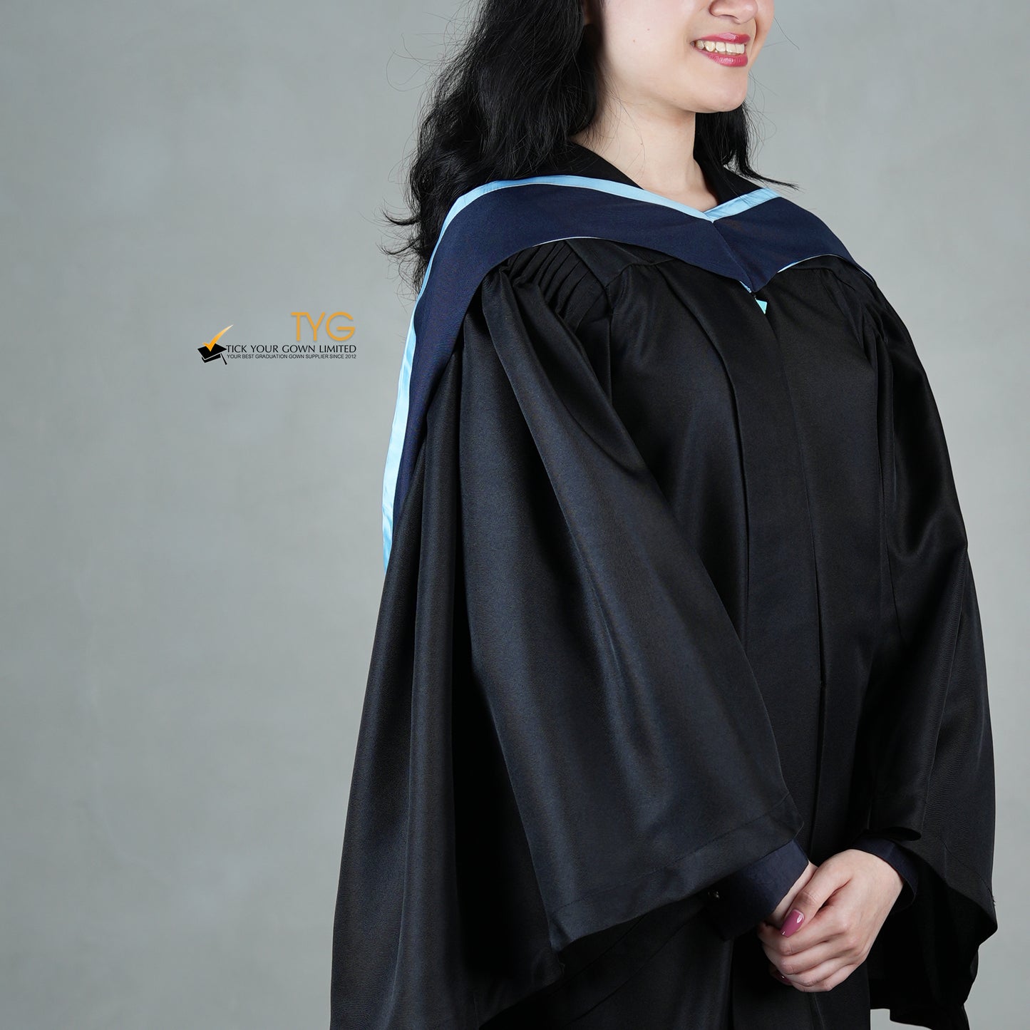 A detailed profile view of a graduate in a black cap and gown with a navy blue hood with light blue lining against a gray background