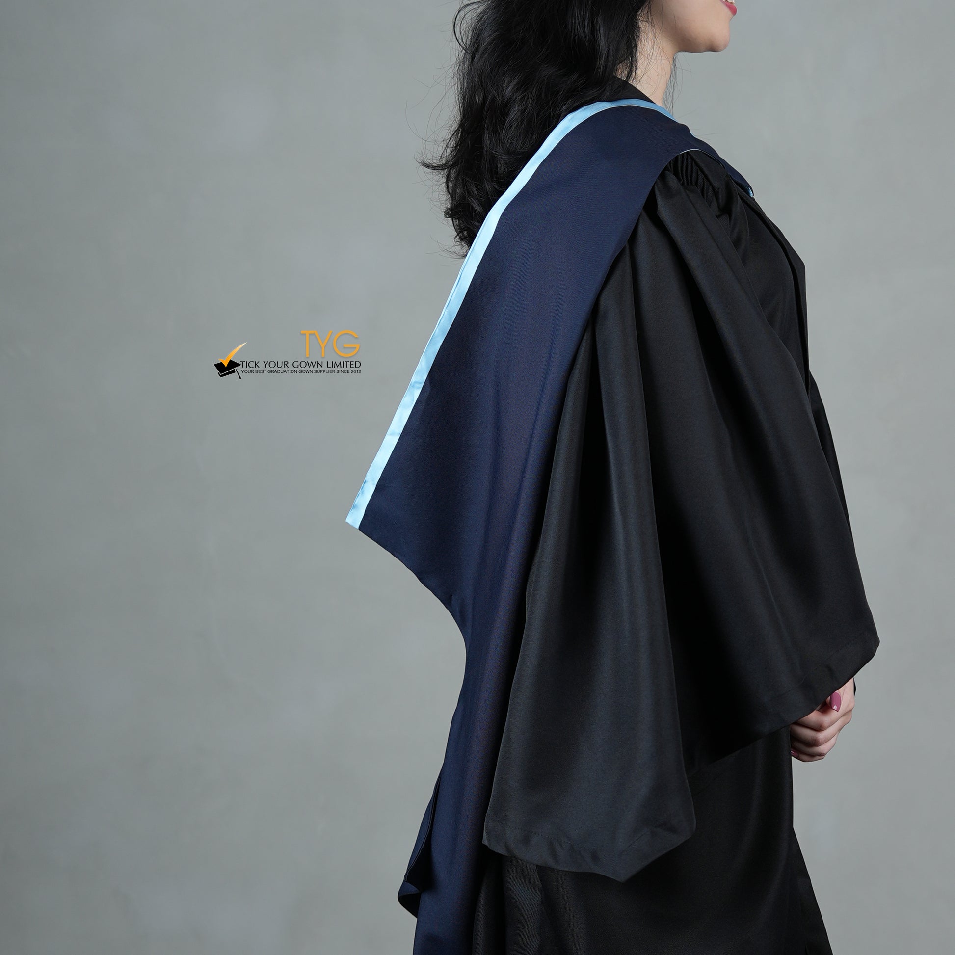 A profile side view of a graduate in a black gown with a navy blue hood with light blue lining against a gray background