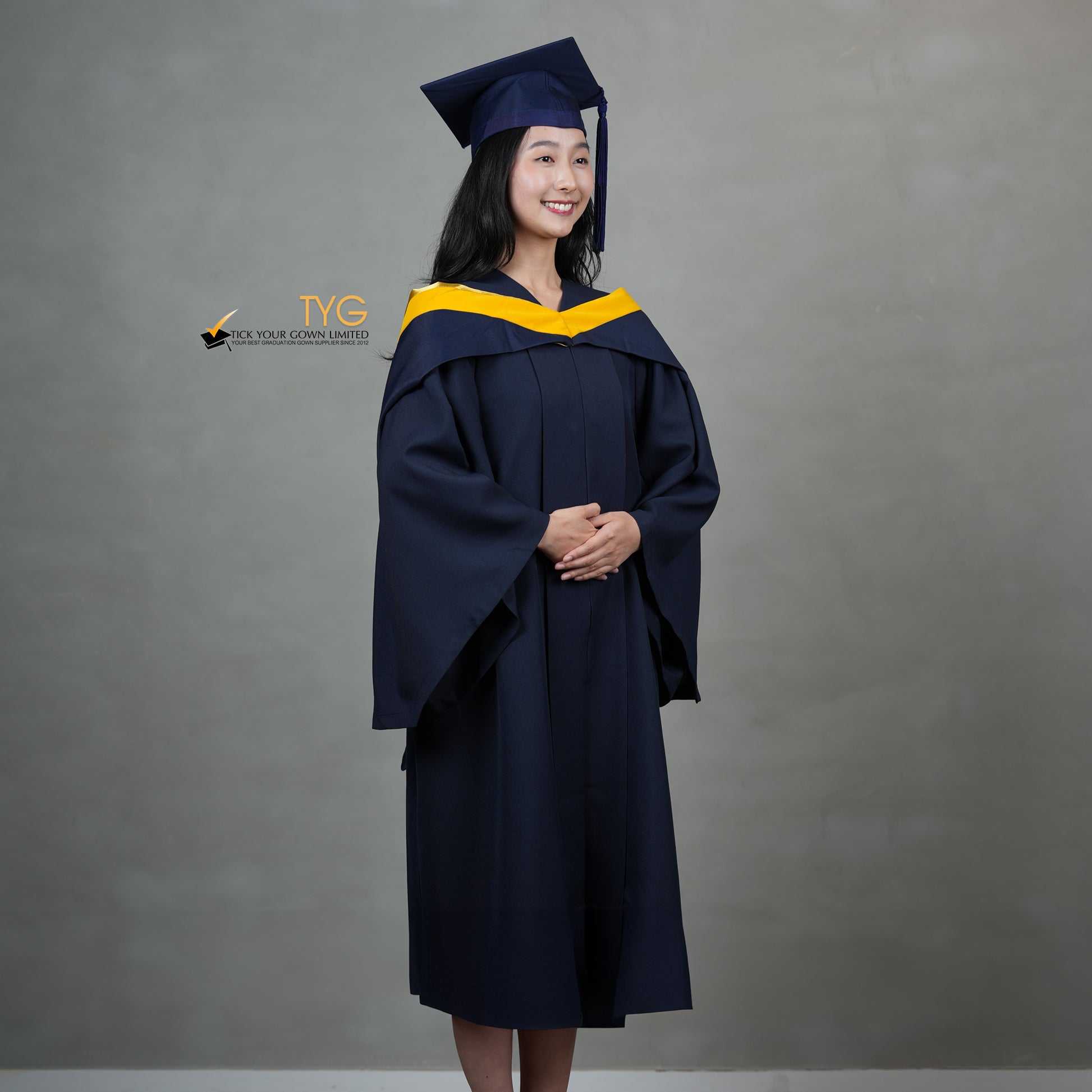 A full profile view of a graduate in a navy cap and gown with a yellow hood against a gray background