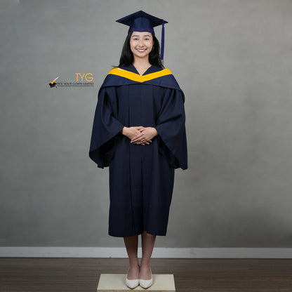 A full front view of a graduate in a navy cap and gown with a yellow hood against a gray background