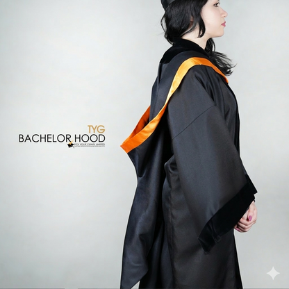 A side view of a graduate in a black graduation gown with an orange bachelor hood against a plain background