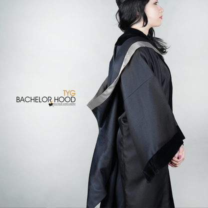 A side view of a graduate in a black graduation gown with a silver bachelor hood against a plain background