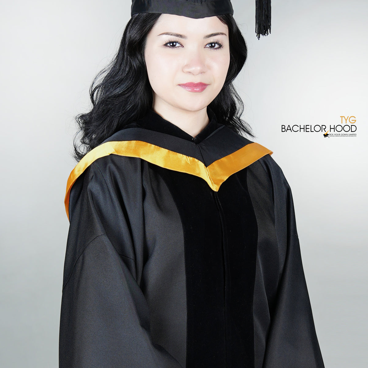 Graduate in black graduation gown with a gold bachelor hood against a plain background