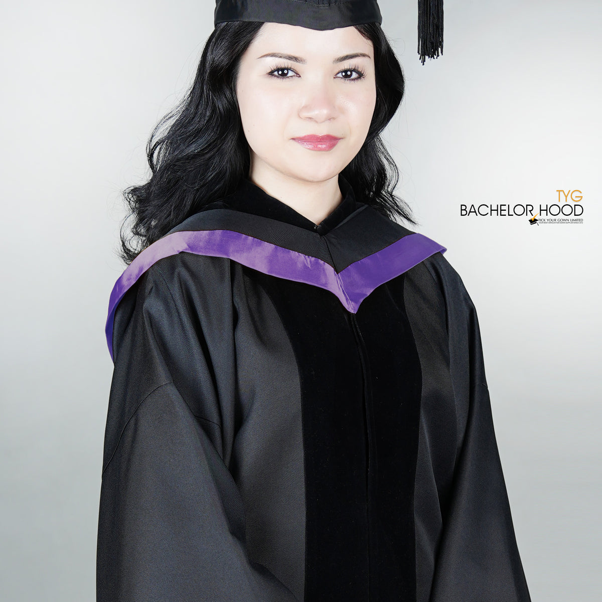 Graduate in black graduation gown with a light purple bachelor hood against a plain background