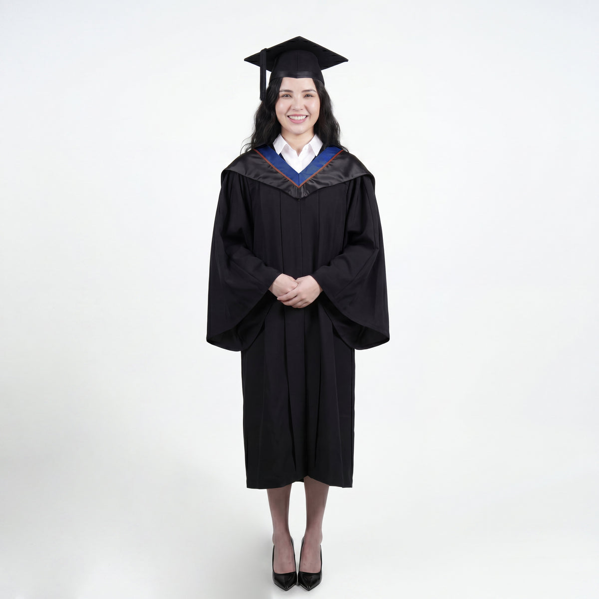 A woman wearing a black graduation gown and matching mortarboard cap stands against a light gray studio background.

The gown has a wide collar with dark blue and brown trim accent hood, and the model is posed with hands clasped in front.