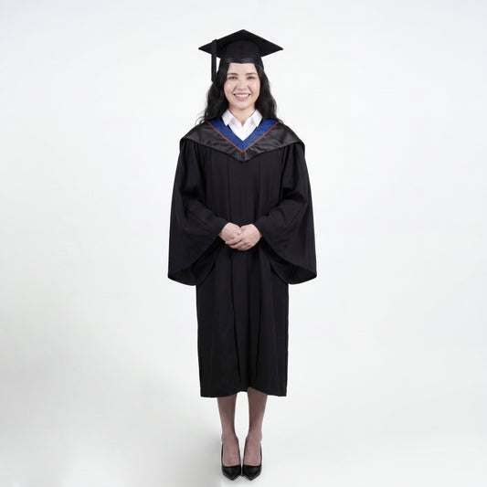 A woman wearing a black graduation gown and matching mortarboard cap stands against a light gray studio background.

The gown has a wide collar with dark blue and brown trim accent hood, and the model is posed with hands clasped in front.