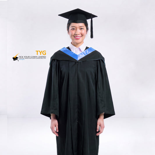 A woman wearing a black graduation gown and a black mortarboard cap stands against a light gray studio background. 

The gown has a light blue bachelor hood, and a white collared shirt is visible underneath.