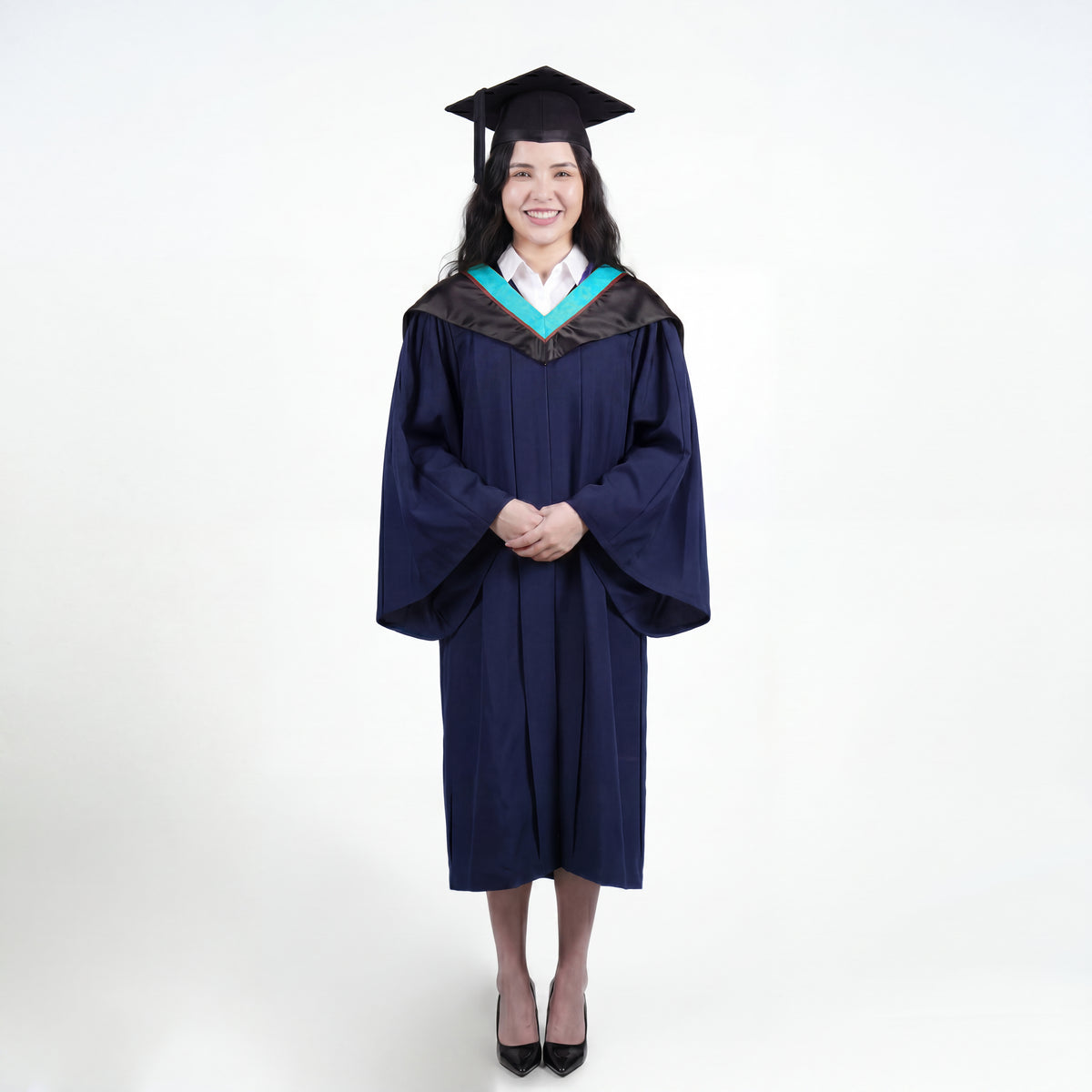 A woman wearing a black graduation gown and matching mortarboard cap stands against a light gray studio background.

The gown has a wide collar with light blue and brown trim accent hood, and the model is posed with hands clasped in front.