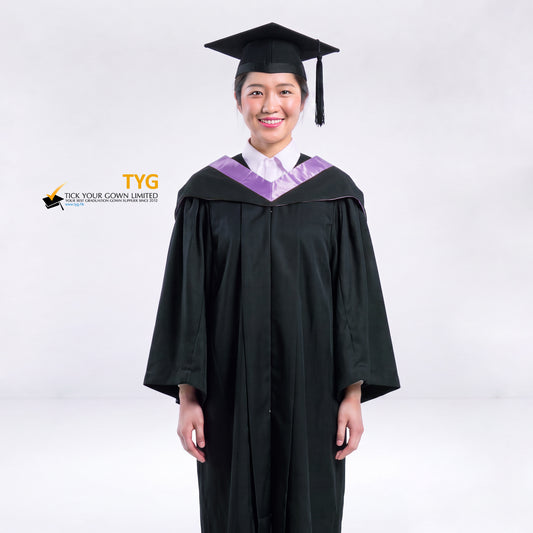 A woman wearing a black graduation gown and a black mortarboard cap stands against a light gray studio background. 

The gown has a lilac bachelor hood, and a white collared shirt is visible underneath.
