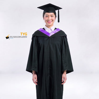 A woman wearing a black graduation gown and a black mortarboard cap stands against a light gray studio background. 

The gown has a purple bachelor hood, and a white collared shirt is visible underneath.
