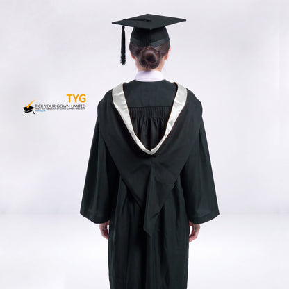 A back view of a woman wearing a black graduation gown and a black mortarboard cap stands against a light gray studio background. 

The gown has a silver bachelor hood, and a white collared shirt is visible underneath.