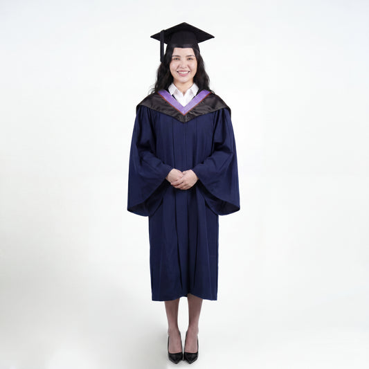 A woman wearing a navy blue graduation gown and matching mortarboard cap stands against a light gray studio background.

The gown has a wide collar with light purple and brown trim accent hood, and the model is posed with hands clasped in front.
