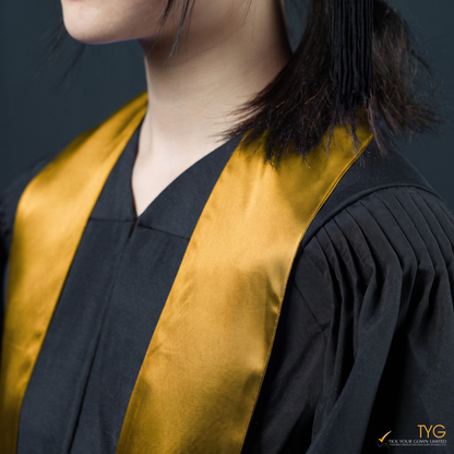 Person wearing a black graduation gown with an orange graduation sash on a dark background