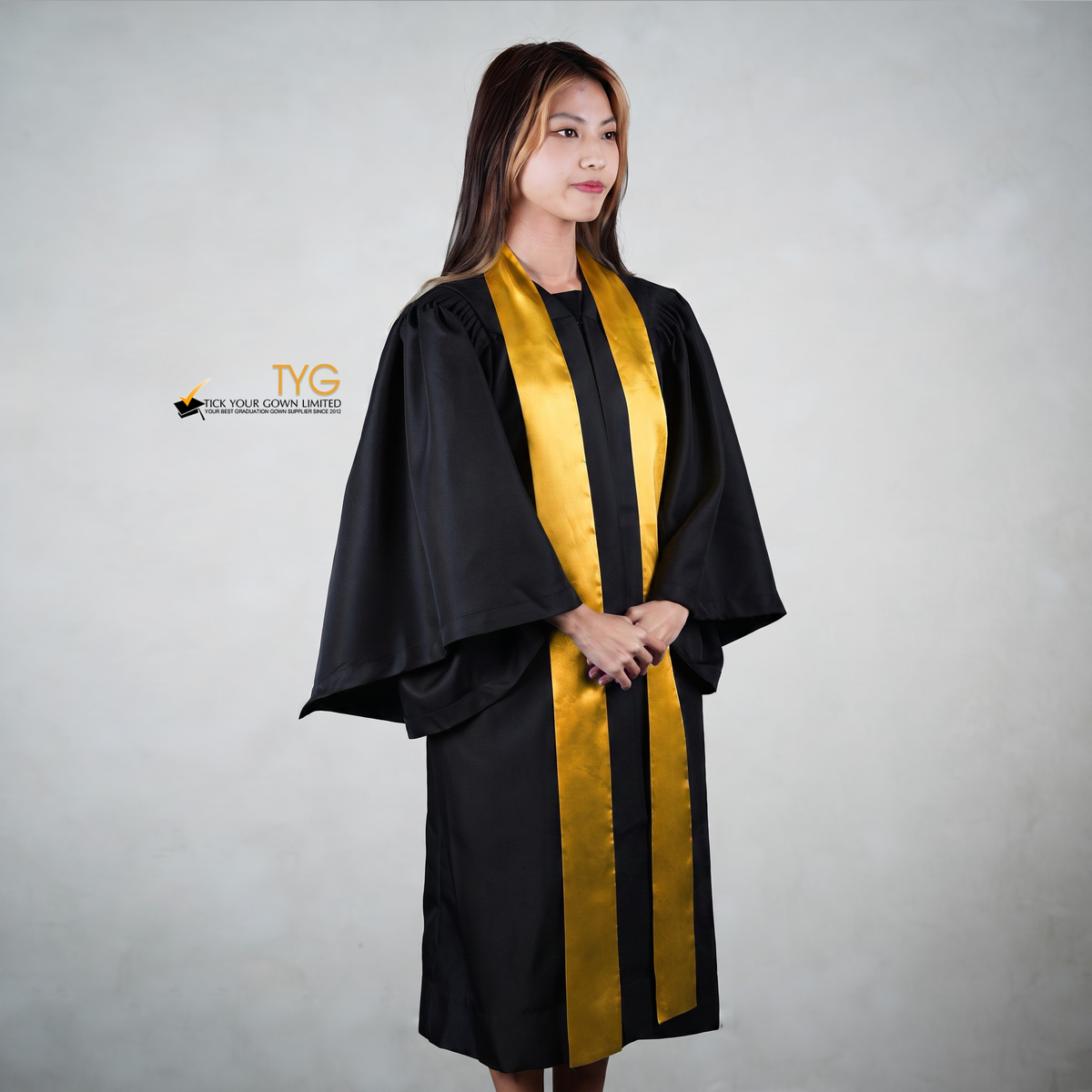 Profile view of a person wearing a black graduation gown with an orange graduation sash on a gray background
