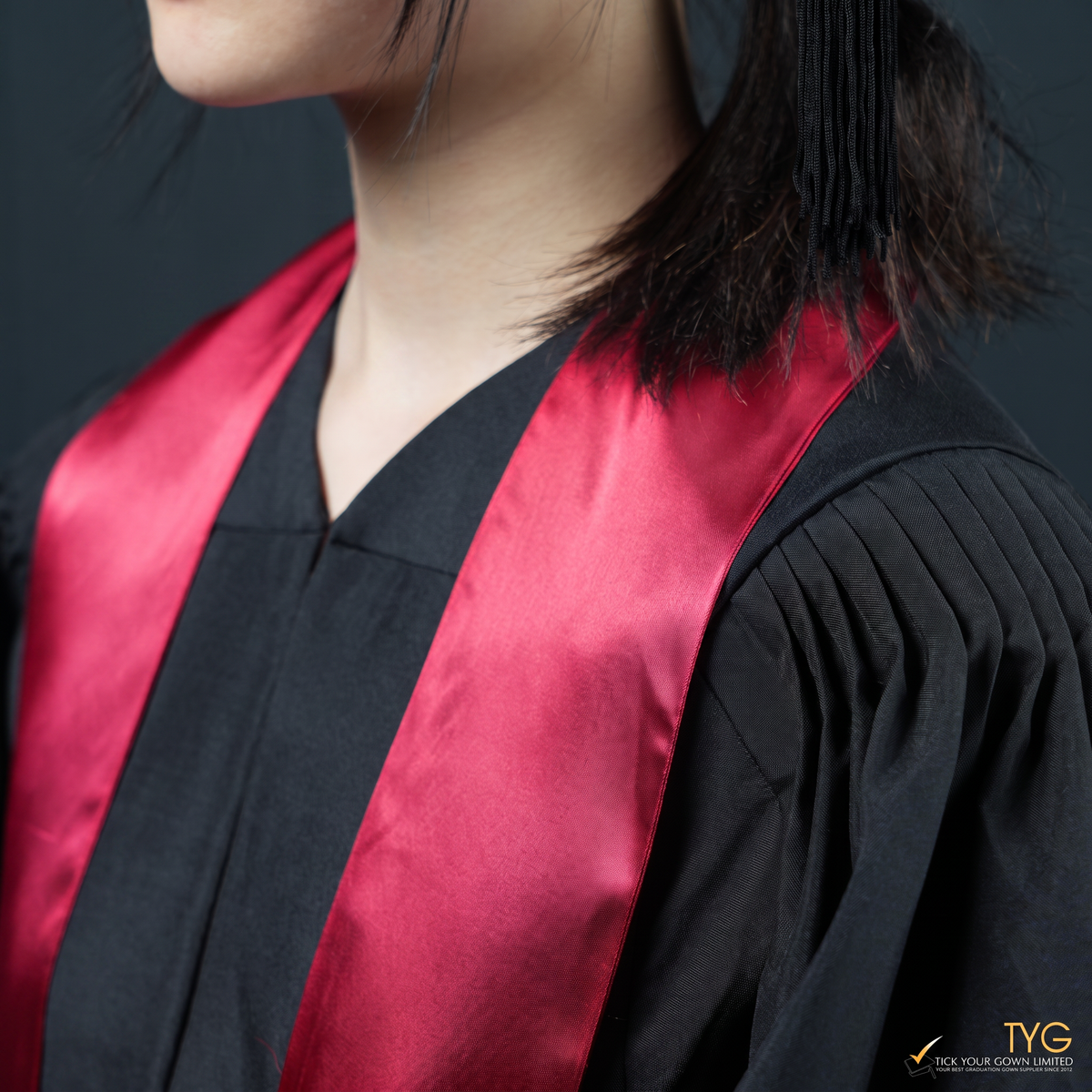 Person wearing a black graduation gown with a red graduation sash on a dark background