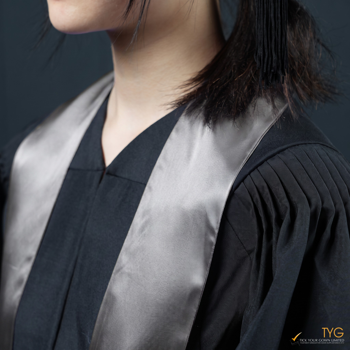 Person wearing a black graduation gown with a silver graduation sash on a dark background