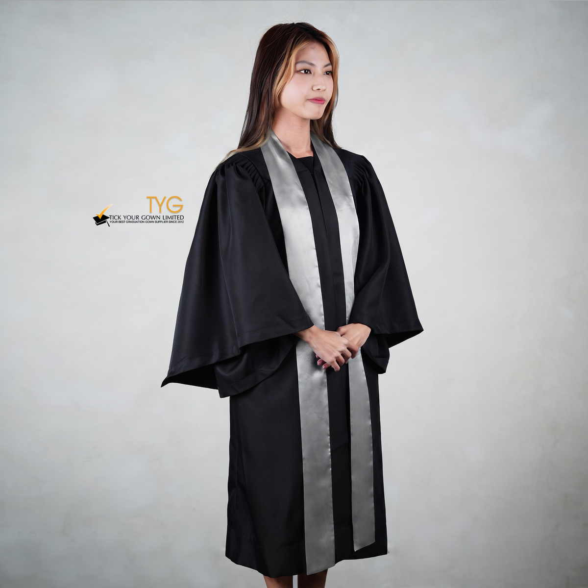 Profile view of a person wearing a black graduation gown with a silver sash on a gray background