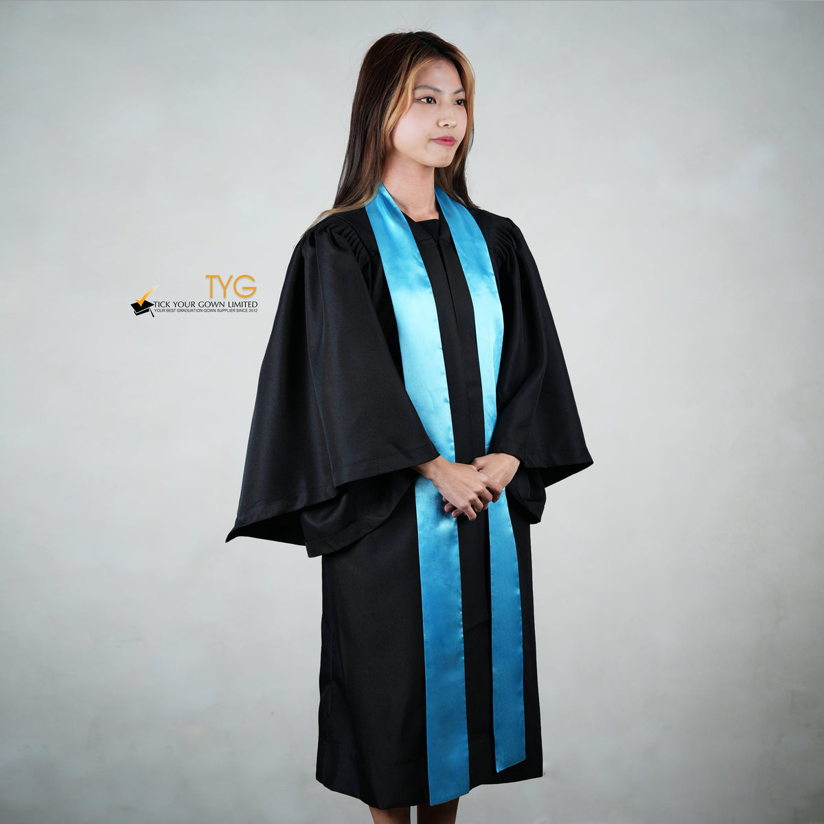 Profile view of a person wearing a black graduation gown with a sky blue graduation sash on a gray background