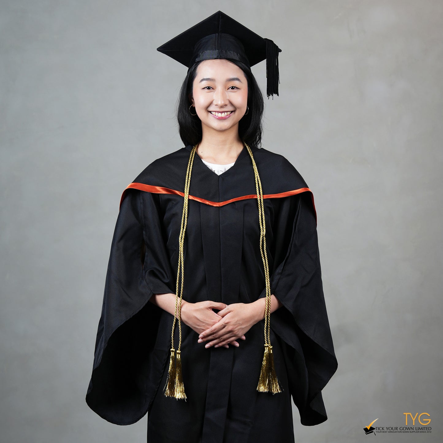 Graduate in black cap and gown with gold honour cords against a gray background