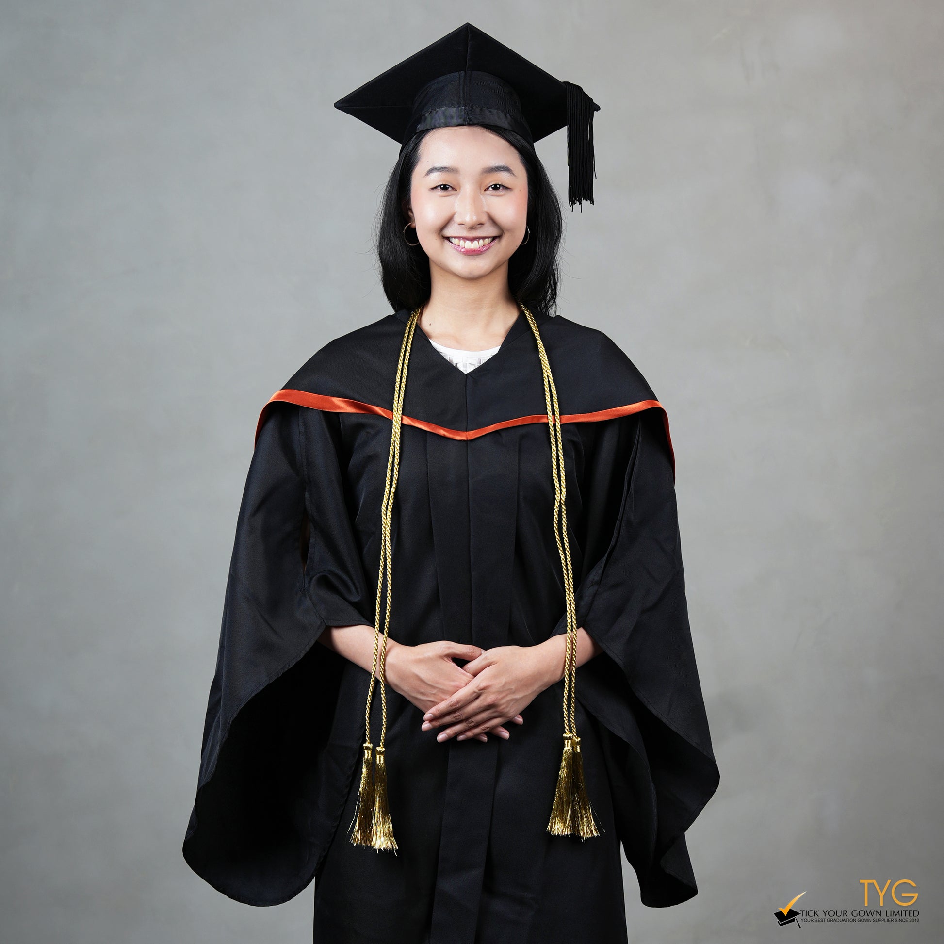 Graduate in black cap and gown with gold honour cords against a gray background