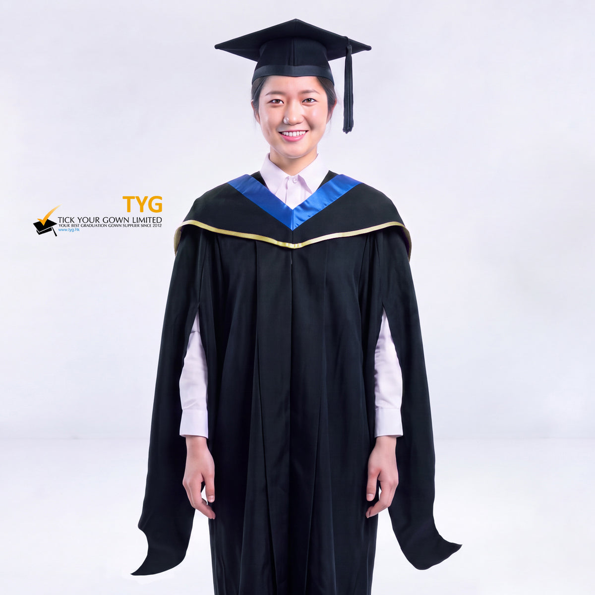 A woman in a black master's graduation gown classic UK with a blue hood with yellow trim accent and with a black mortarboard cap with an black tassel against a gray background.