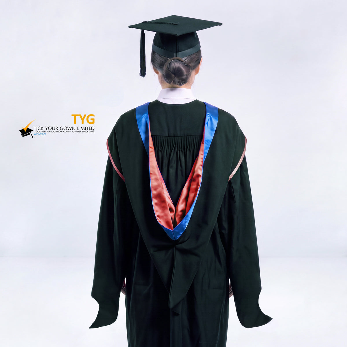 A back view of a woman in a black master's graduation gown classic UK with a blue hood with red trim accent and with a black mortarboard cap with a black tassel against a gray background.