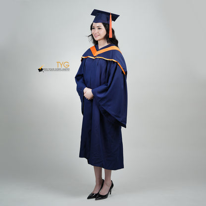 A full body profile shot of a person in a navy blue graduation gown and an orange hood and with a mortarboard cap with an orange tassel against a gray background.