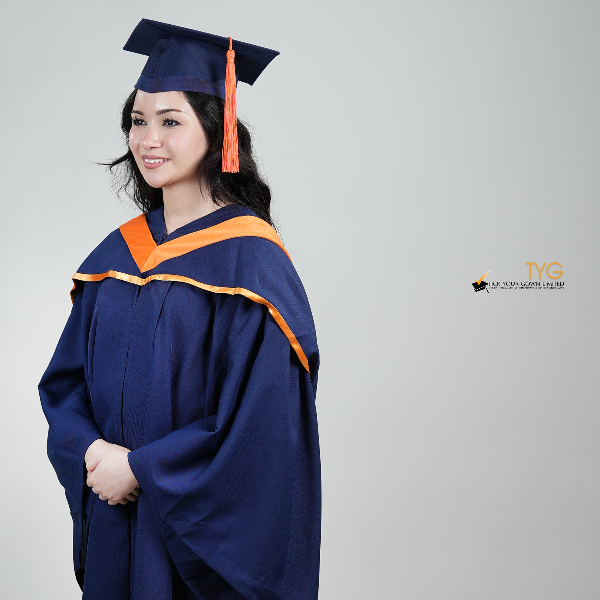 A profile view of a person in a navy blue graduation gown and an orange hood and with a mortarboard cap with an orange tassel against a gray background.