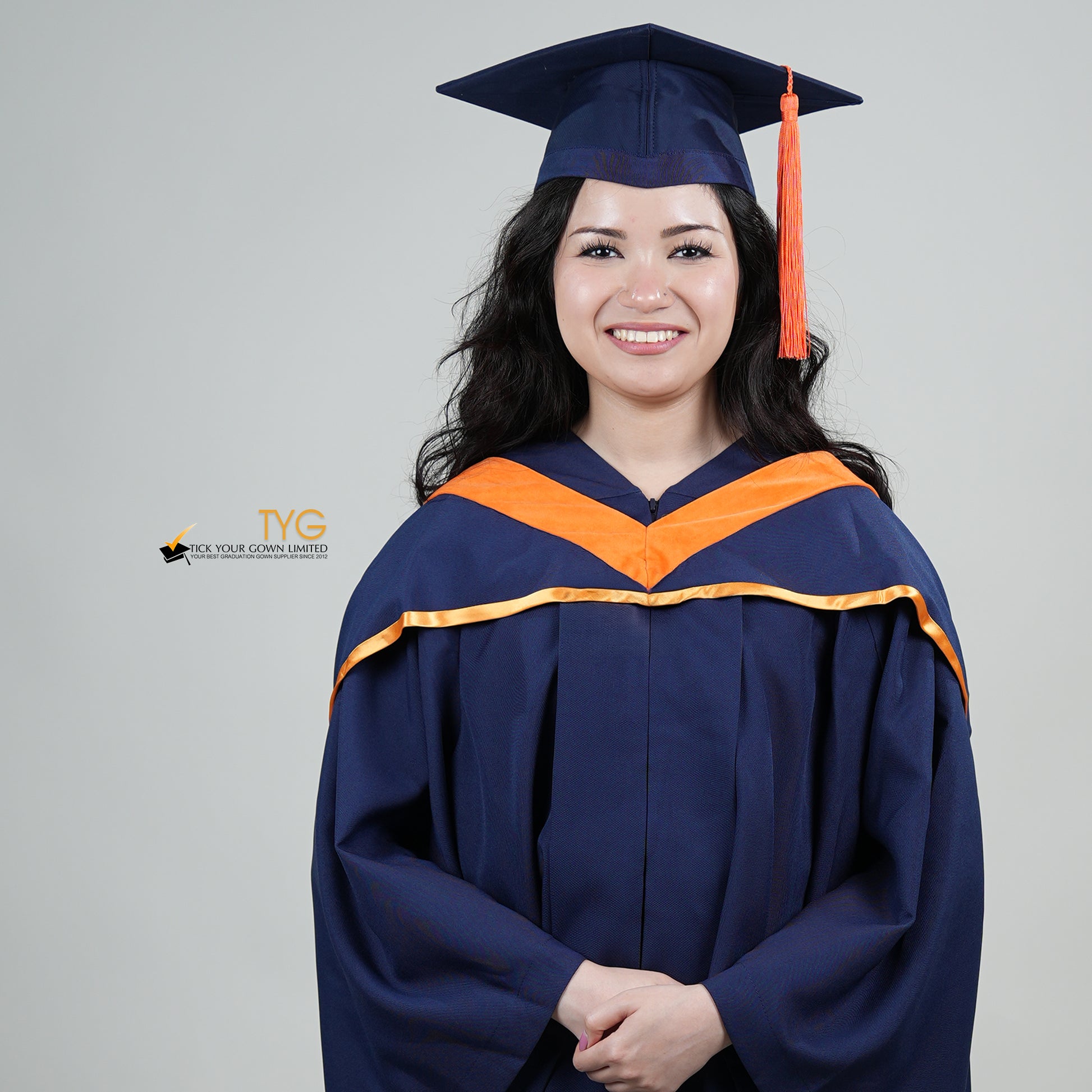 A person in a navy blue graduation gown and an orange hood and with a mortarboard cap with an orange tassel against a gray background.