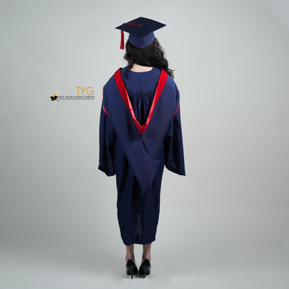 A full body shot of a person in a navy blue graduation gown and a red hood and with a mortarboard cap with a red tassel against a gray background.