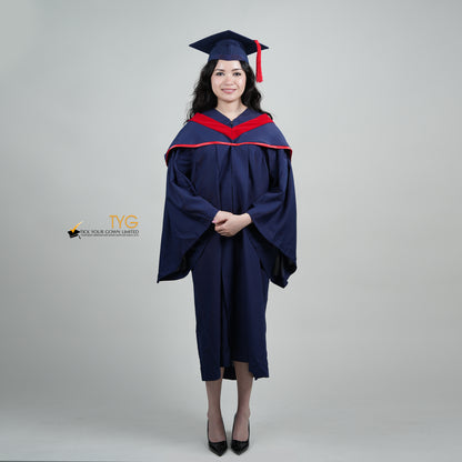 A full body shot of a person in a navy blue graduation gown and a red hood and with a mortarboard cap with a red tassel against a gray background.