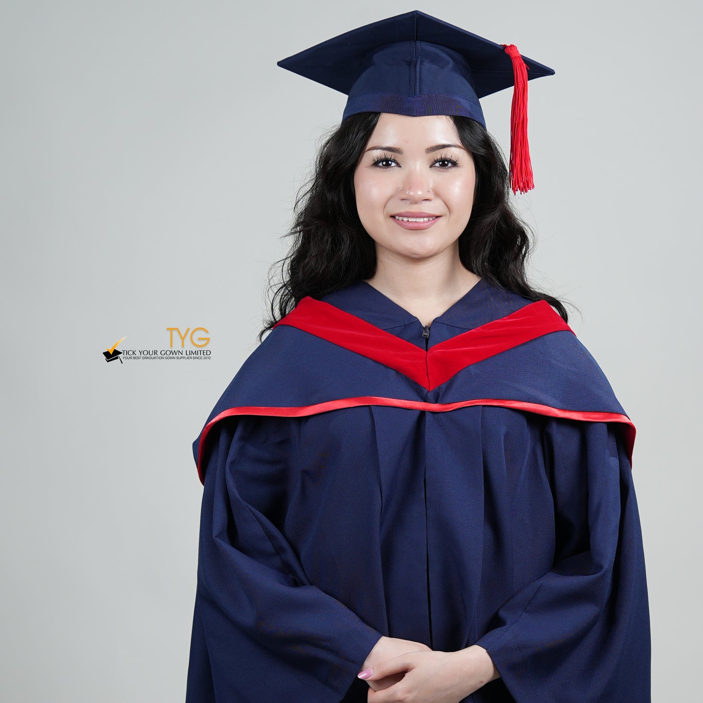 A person in a navy blue graduation gown and a red hood and with a mortarboard cap with a red tassel against a gray background.
