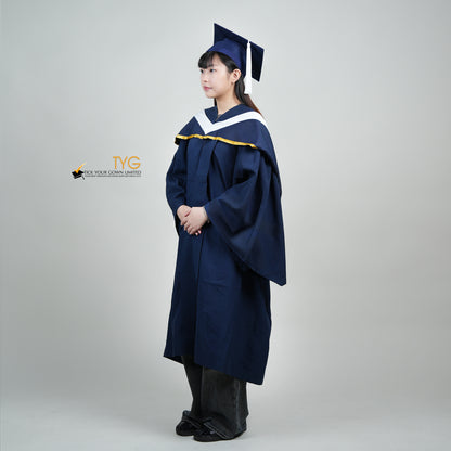 A full body profile view of a person in a navy blue graduation gown and a white hood with gold lining and with a mortarboard cap with a white tassel against a gray background.