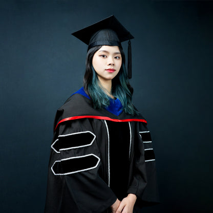 Profile view of a person wearing a black masters graduation gown with silver striped sleeves, a blue-and-red satin hood, and a mortarboard cap with a black tassel.