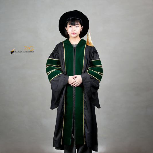 Front view of a person wearing a PhD graduation gown in black with forest green velvet panels, matching sleeve bars, gold trim, and a matching doctoral bonnet with gold tassel.