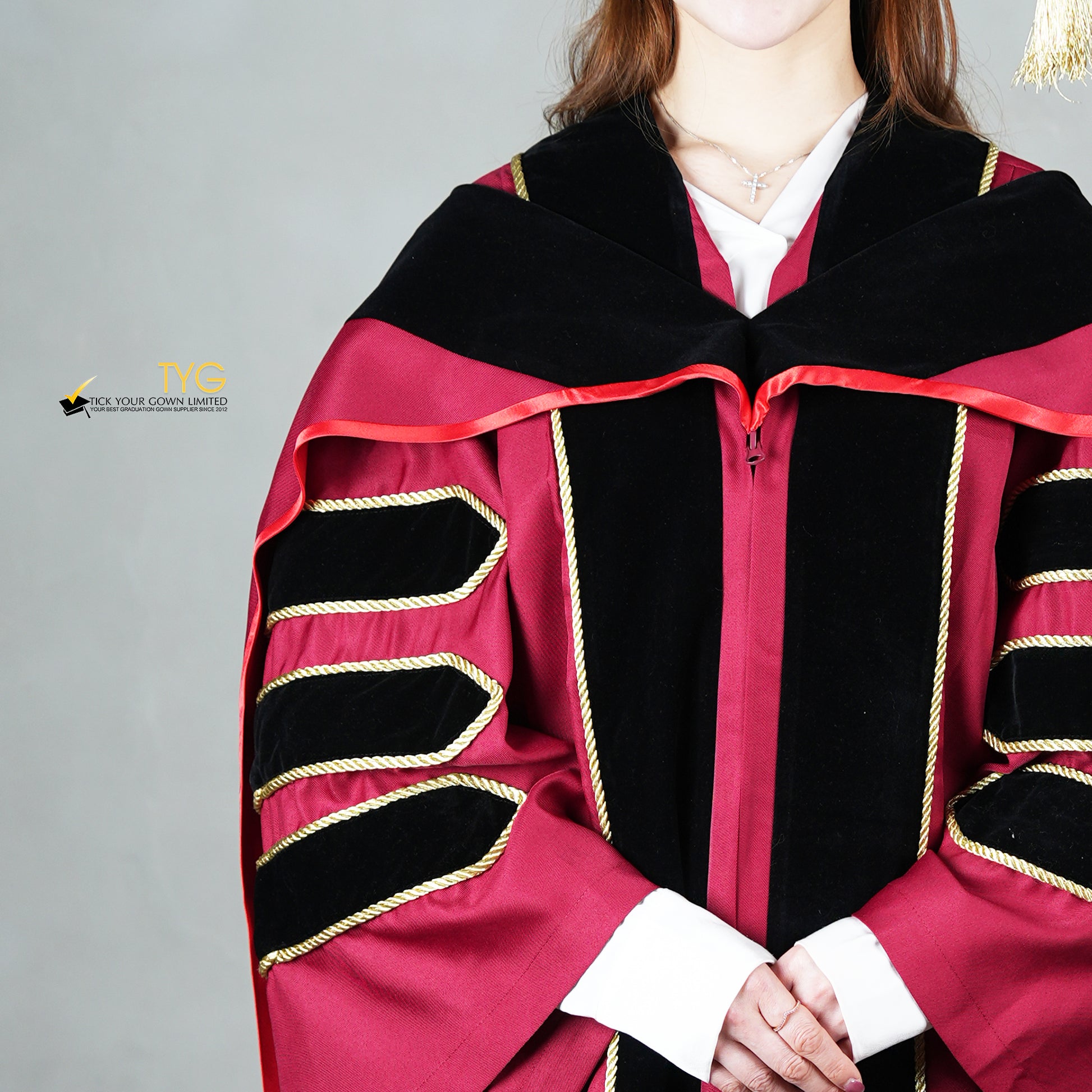 A detailed view of a person wearing a doctoral graduation gown in maroon with black velvet panels, matching black velvet sleeve bars in gold trim