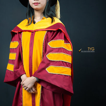 A detailed profile view of a person wearing a classic PhD graduation gown in maroon with yellow velvet panels, matching sleeve bars, and a black doctoral bonnet with gold tassel