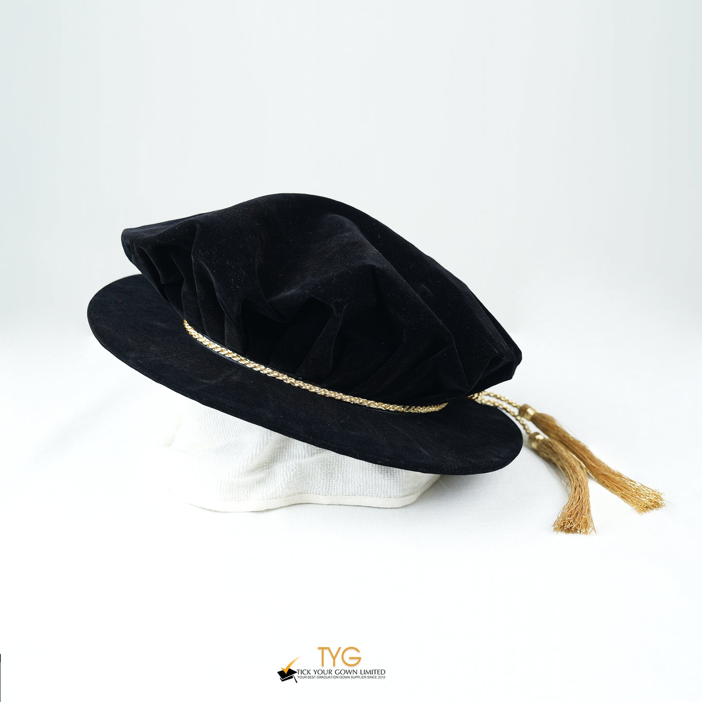 Black velvet hat with gold trim and tassel on a white background.