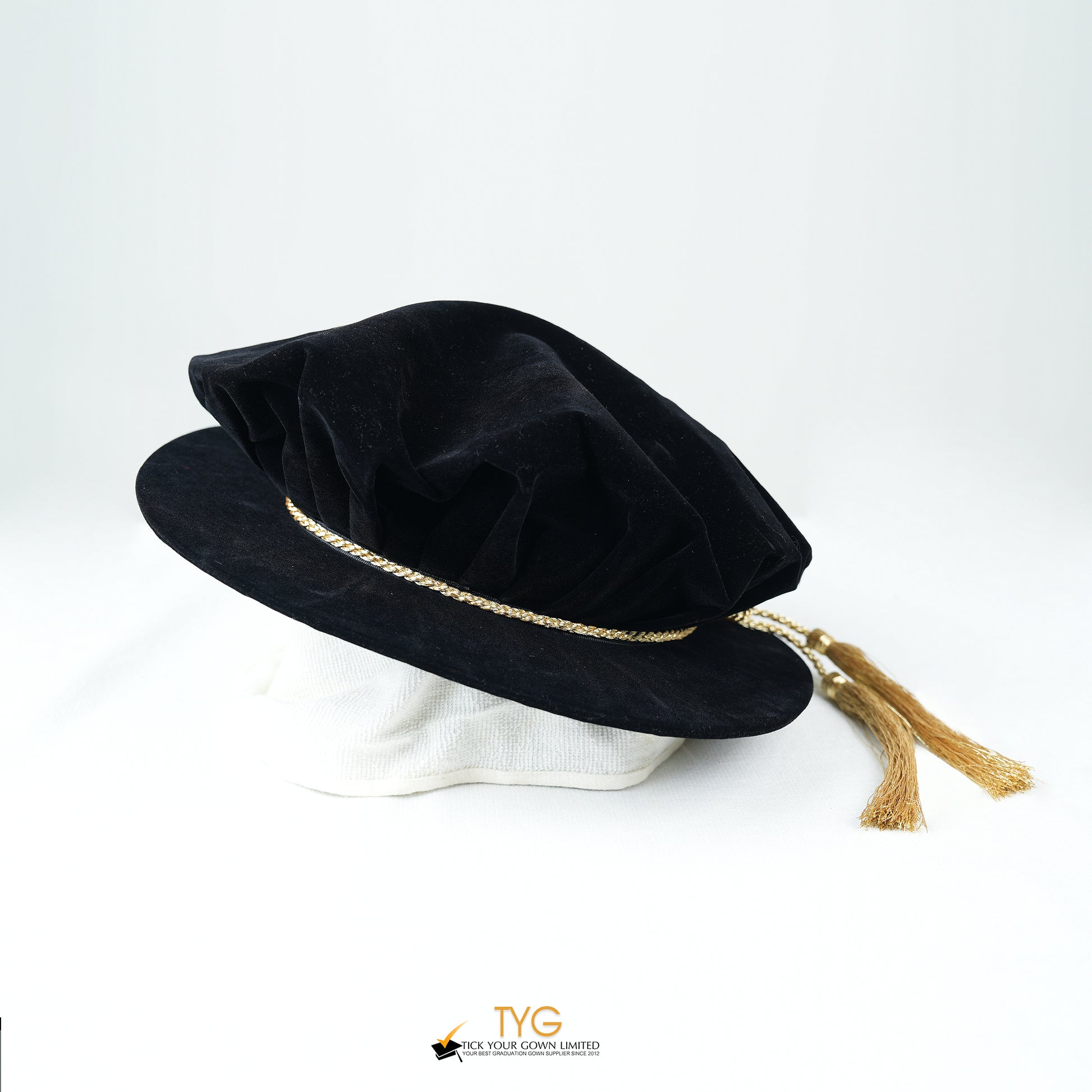 Black velvet hat with gold trim and tassel on a white background.